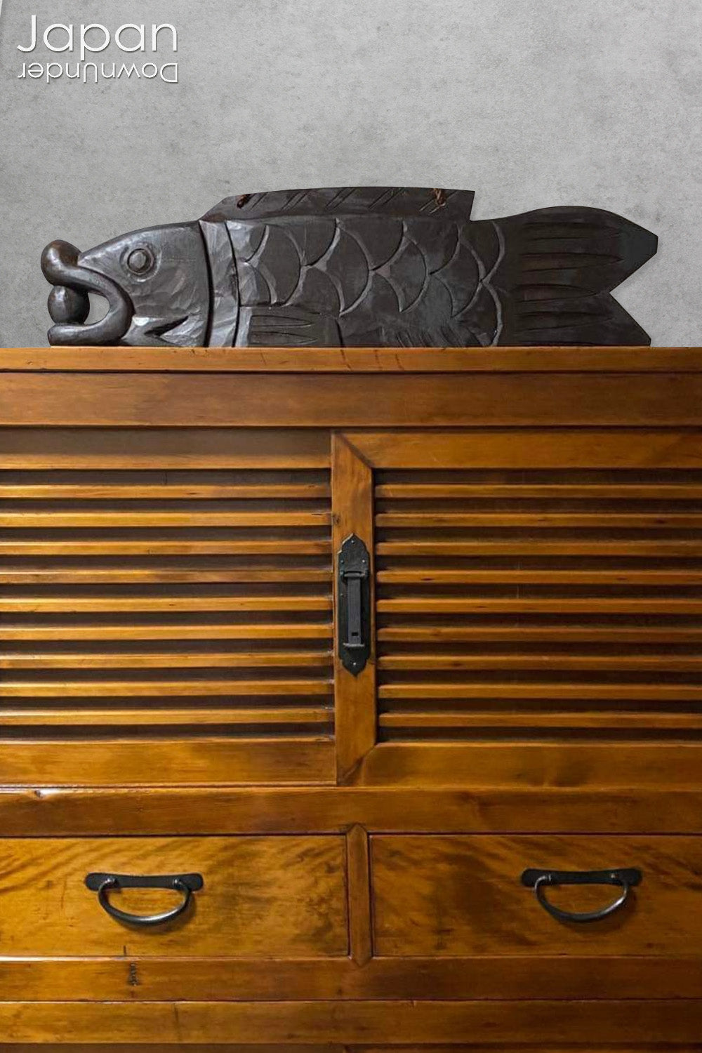 A vintage Buddhist temple gyoban; a  plank of wood shaped like a fish.  It is carved from   wood. The scales, big eye and fin, etched  into the wood,  give the fish form. There is a  round pearl in the fish mouth,  symbolizing unity.