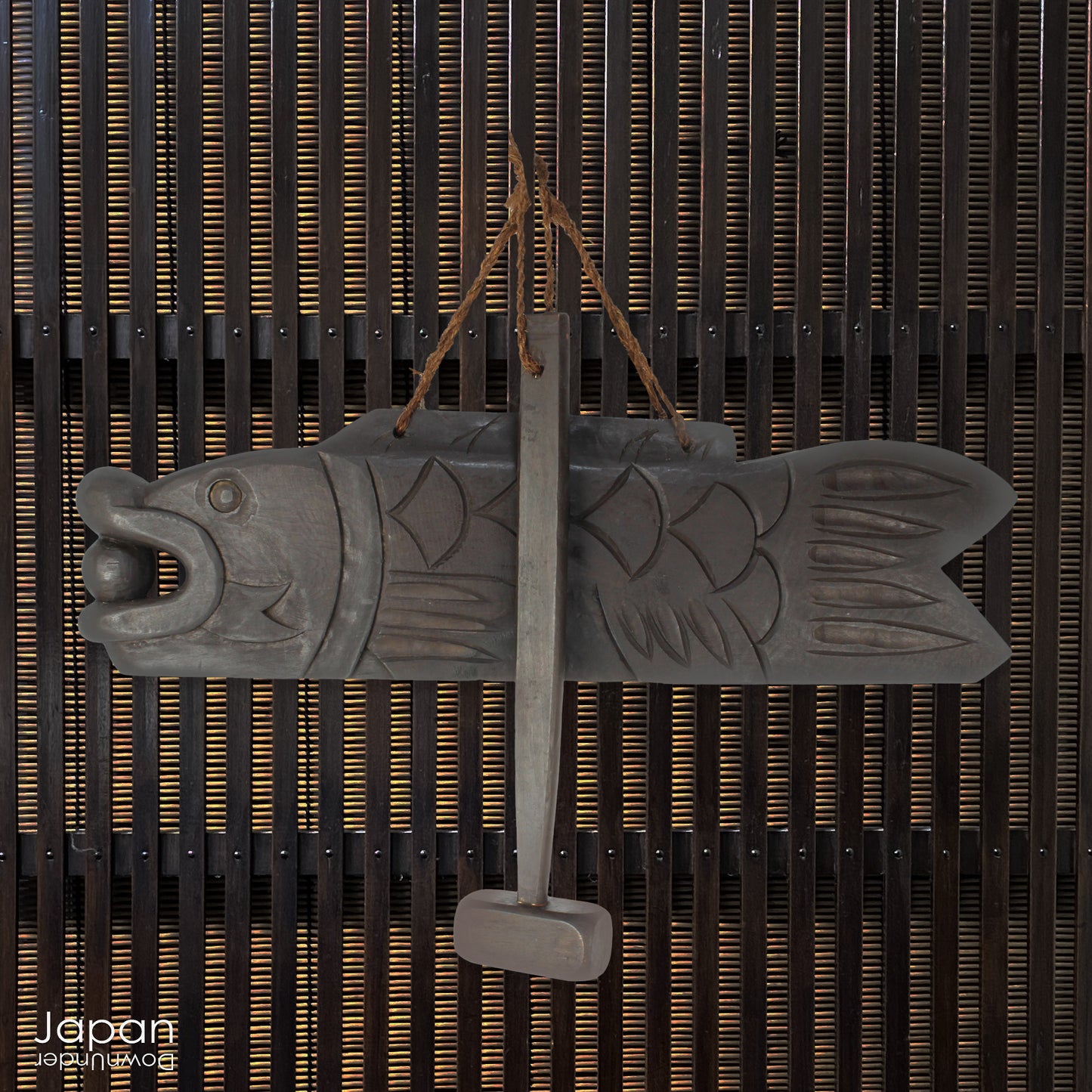 A vintage Buddhist temple gyoban; a  plank of wood shaped like a fish.  It is carved from   wood. The scales, big eye and fin, etched  into the wood,  give the fish form. There is a  round pearl in the fish mouth,  symbolizing unity.