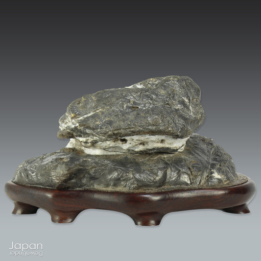 Immerse yourself in the meditative beauty of this captivating miniature suiseki - a traditional Japanese art form where nature is the true sculptor. Gracefully resting on a finely hand-carved ebony daiza (base), this stone embodies stillness and quiet strength, making it an ideal centerpiece for contemplative spaces, creative corners, or serene interiors.