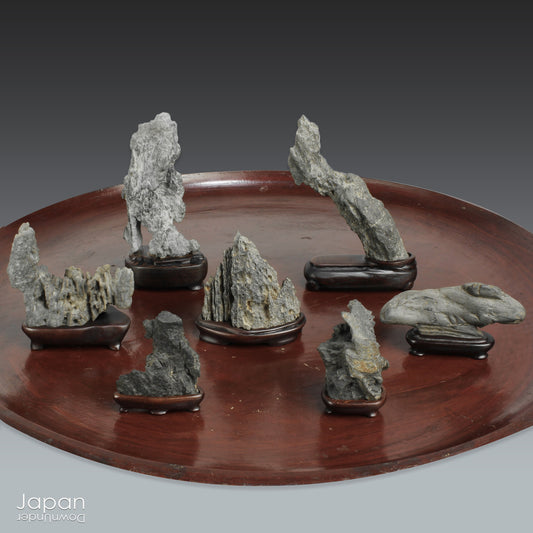 Invite serenity and understated beauty into your space with this remarkable collection of seven vintage miniature Japanese suiseki - natural “water stones” cherished for their quiet symbolism and evocative forms. Each small stone rests atop a finely hand-carved ebony daiza (stand), thoughtfully crafted to support and elevate its unique presence.