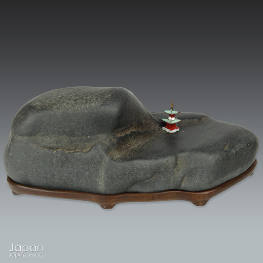 Introduce a quiet elegance and poetic depth to your space with this vintage Japanese suiseki - a contemplative stone shaped by nature and imbued with a serene, spiritual aura. Resting on a finely hand-carved daiza (wooden base) and accompanied by a small metal pagoda, this piece emanates stillness, balance, and an understated visual allure.