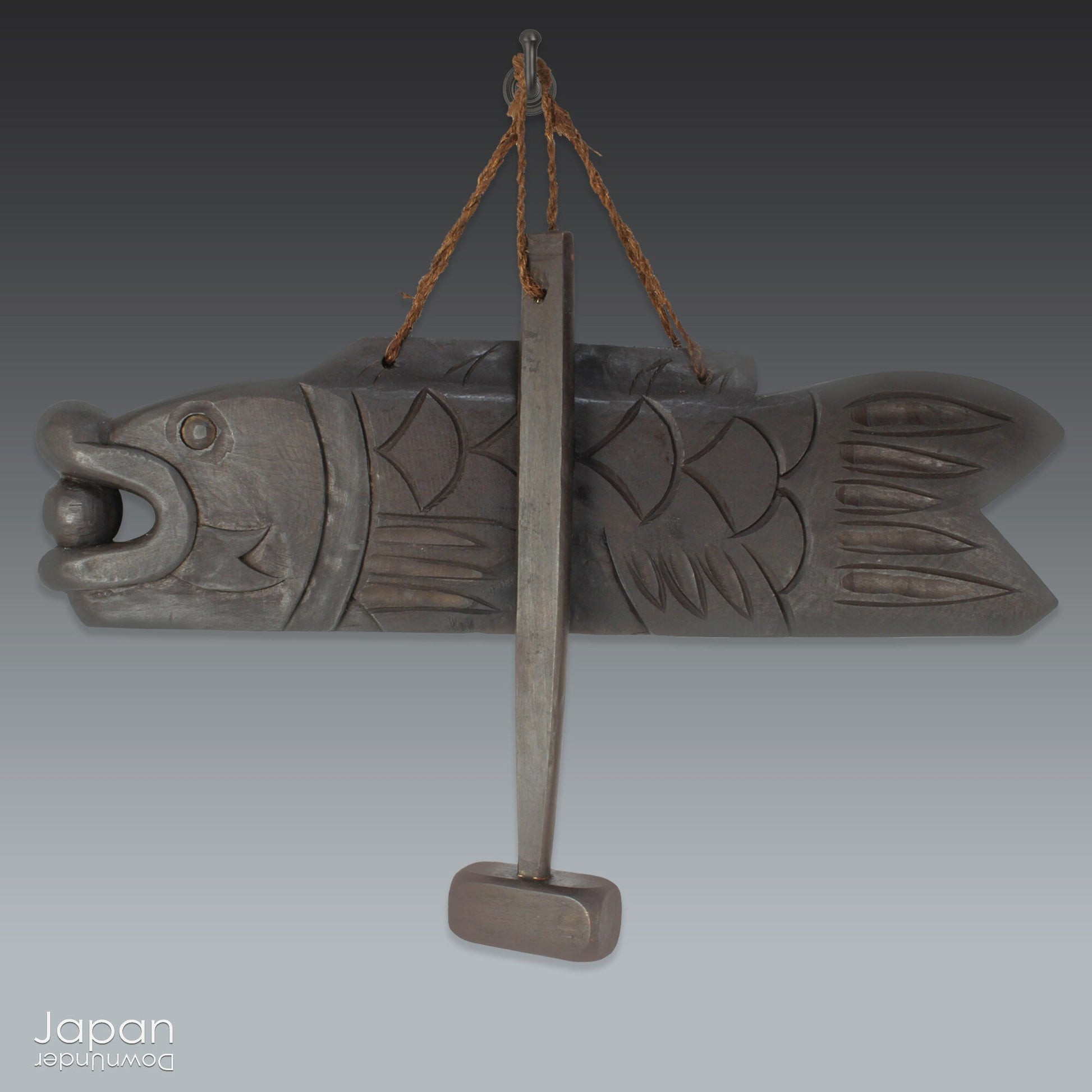 A vintage Buddhist temple gyoban; a  plank of wood shaped like a fish.  It is carved from   wood. The scales, big eye and fin, etched  into the wood,  give the fish form. There is a  round pearl in the fish mouth,  symbolizing unity.