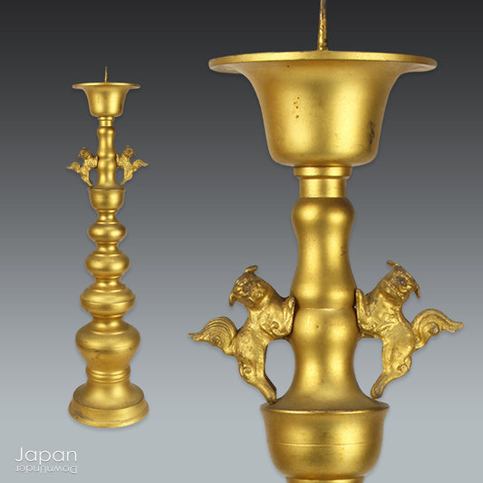An antique Buddhist temple candle holder.    The gilded brass candle holder is a cylindrical shape, formed of spheres,  gradually decreasing in size as they move upwards. Just below the candle cup hang a pair of Japanese komainu, or lion dogs.